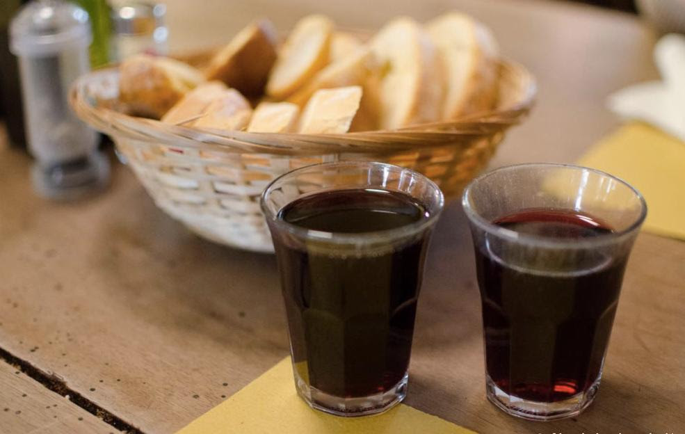 Short glasses of red wine on a rustic table with a basket of bread 